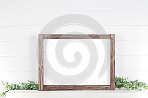 Mock up A4 horizontal frame made of rough wood with on a shelf with greens