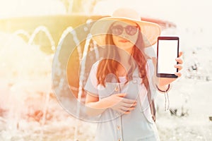 Mock up. Beautiful young woman in a hat and glasses holding a the phone. Isolate. A fountain in the background. Close up