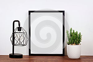Mock up black frame against white wall with cactus and lamp on a wood shelf