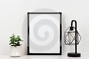 Mock up black frame against white wall with succulent plant and lamp on a white shelf