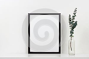 Mock up black frame against white wall with vase of branches on a white shelf