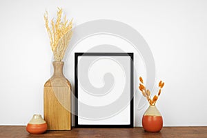 Mock up black frame with autumn branches and decor on a wood shelf