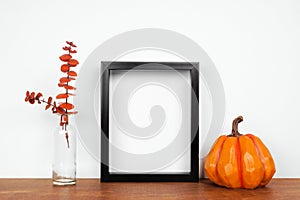 Mock up black frame with autumn branches and pumpkin decor on a wood shelf