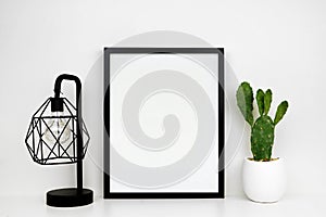 Mock up black frame, cactus plant and industrial style lamp on a white shelf or desk against a white wall