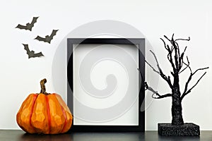 Mock up black frame with Halloween pumpkin and spooky tree decor on a shelf against a white wall