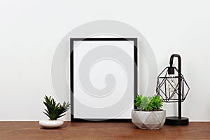 Mock up black frame against white wall with succulent plants and lamp on a wood shelf