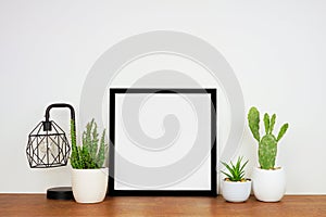 Mock up black square frame with home decor and potted plants wih wood shelf and whitewall