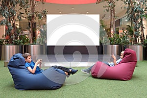 Mock up. Blank advertising screen in modern shopping mall. Children with mobile phone near big blank digital screen