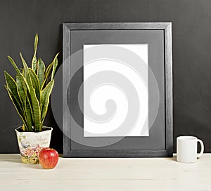 Mock up of blank photo frame with plant pot, mug and apple on wooden shelf.