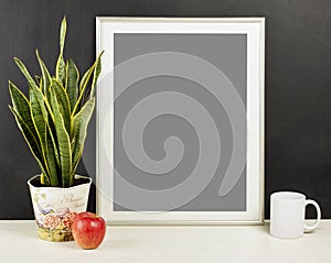 Mock up of blank photo frame with plant pot, mug and apple on wooden shelf.