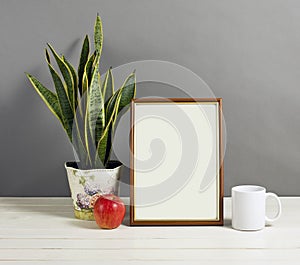 Mock up of blank photo frame with plant pot, mug and apple on wooden shelf.