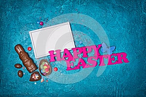 Mock up of blank white frame with pink text of happy easter and traditional sweets as chocolate bunny