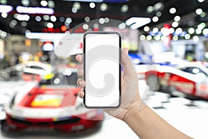 Mock up blank white screen mobile phone for automotive advertisement. Hand holding smartphone with Blurred image of super cars and