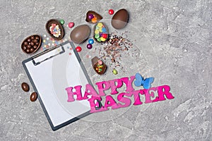 Mock up of clipboard with pink text of happy easter and chocolate traditional eggs