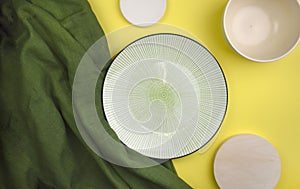 Mock up composition with empty ceramic tableware, green fabric on yellow background.