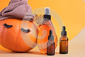 mock up cosmetic containers and pumpkin with towel and eyelashes on orange background, natural skin care in autumn