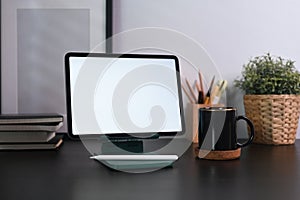 Digital tablet, coffee cup, picture frame and houseplant on black table.