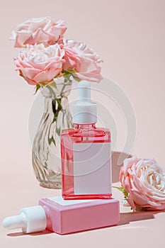 Mock-up of a dropper bottle in sunlight against rose bunch. Shadow of bottle falls on pink background. Concept of beauty