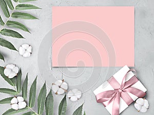 Mock up empty pink paper blank with gift box,  cotton flowers and leaves on grey textured  background.