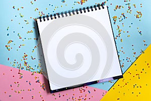 Mock up of empty spiral scketchbook with white paper on bright vibrant background with colorful confetti . Copy space.