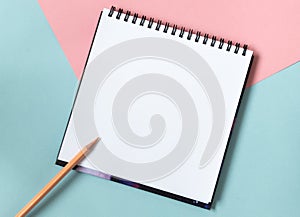 Mock up of empty spiral sketchbook with white paper on pastel pink and blue background. Top view of open notebook with