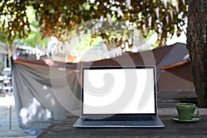 Laptop computer with blank screen on folding picnic table near camp tent outdoors.