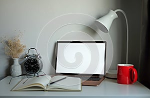 Mock up laptop computer, book, coffee cup and lamp on white table in comfortable home