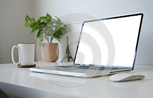 Mock up laptop computer, coffee cup and potted plant on white table. Empty screen for your advertise text