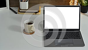 Mock up laptop computer, cup go coffee and supplies on white working desk. Empty screen for your advertise text