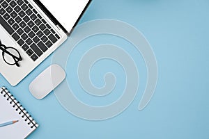 Laptop computer, wireless mouse and notebook on blue background.