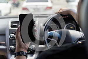 Mock up of man using mobile smart phone inside a car. Driver hand holding blank black screen smartphone, searching address