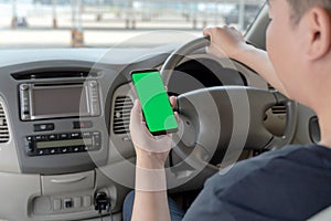 Mock up of man using mobile smart phone inside a car. Driver hand holding blank green screen smartphone, searching address and pin