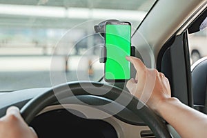 Mock up of man using mobile smart phone inside a car. Driver hand holding blank green screen smartphone, searching address and pin