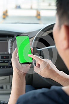 Mock up of man using mobile smart phone inside a car. Driver hand holding blank green screen smartphone, searching address and pin