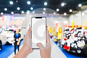 Mock up mobile phone. Hand holding mobile phone with abstract blurred cars exhibition show background image. Car shopping online,