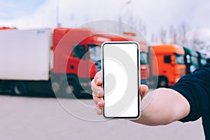 Mock up a smartphone in the hand of a man. Against the background of red trucks. Logistics concept