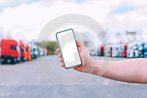 Mock up a smartphone in the hand of a man. Against the background of red trucks. Logistics concept.