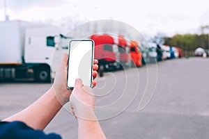 Mock up a smartphone in the hands of a man. Against the background of red trucks. Logistics concept