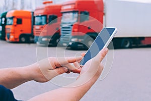 Mock up a smartphone in the hands of a man. Against the background of red trucks. Logistics concept