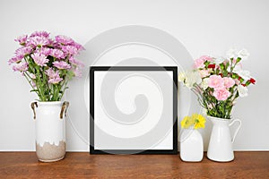 Mock up square frame with vases of colorful flowers. Wooden shelf against a white wall.