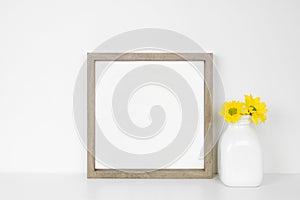 Mock up square frame with yellow daisy flowers. White shelf against a white wall.