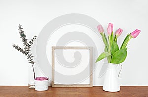 Mock up square wood frame with plant, branches and flowers. Wooden shelf against a white wall.