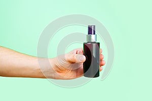 Mock-up of unbranded brown plastic spray bottle and male hand on green background. Cosmetic bottle container for branding of