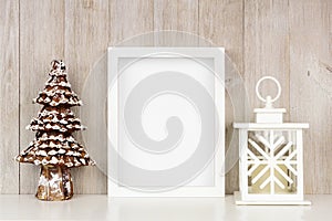 Mock up white frame with Christmas tree and lantern decor on a shelf against a rustic gray wood wall