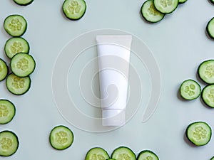 Mock-up of white squeeze cosmetic tube and fresh cucumber slices on pale green background. Top view. Moisturizing cosmetics