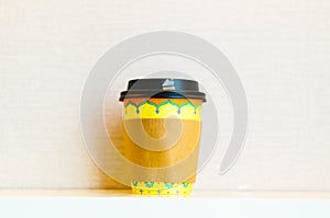 Mock-up of a yellow take away cup of coffee in the center with a brown heat insulation paper