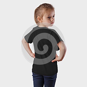 Mockup black children`s t-shirt on a posing girl in blue jeans, on a background in the studio