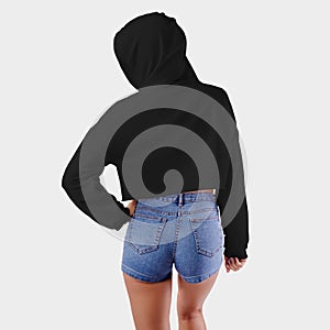 Mockup black crop top on a girl in a hood with a hand on her belt, standing backwards, for presentation of design, pattern, logo