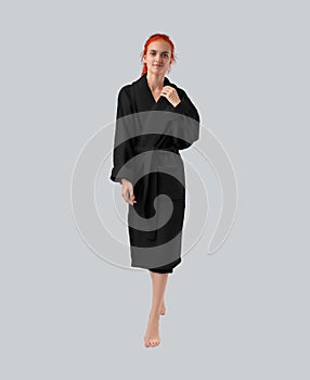 Mockup of a black terry bathrobe with a belt on a full-length red-haired girl, a winter robe with rolled-up sleeves, front view