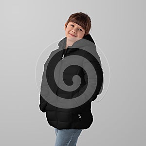 Mockup of a black winter puffer jacket on a child, garment zippers up, hands in pockets, front view, space for design, branding